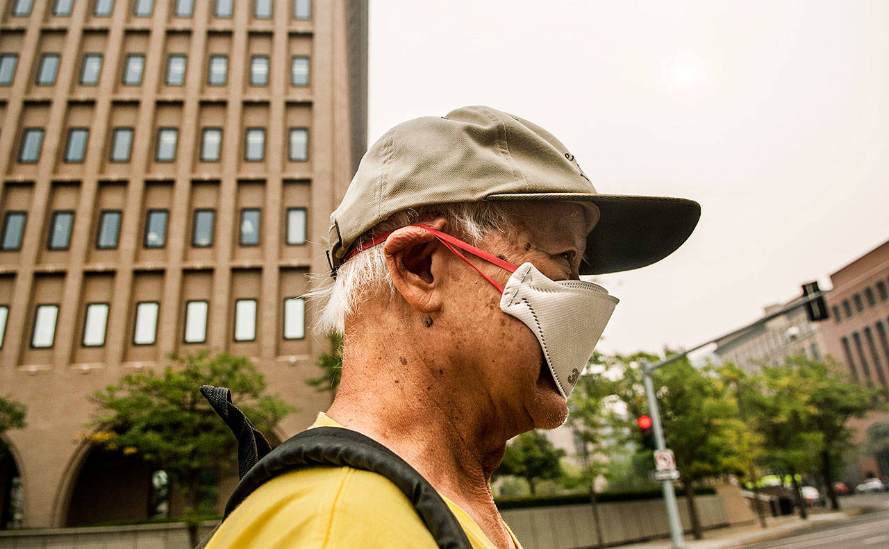 Bill Leong covers his face as a smoke fills Spokane on Tuesday. The growing blaze east of Portland in the scenic Columbia River Gorge was one of dozens of wildfires in the U.S. West that sent smoke into cities from Seattle to Denver. (Kathy Plonka/The Spokesman-Review via AP)