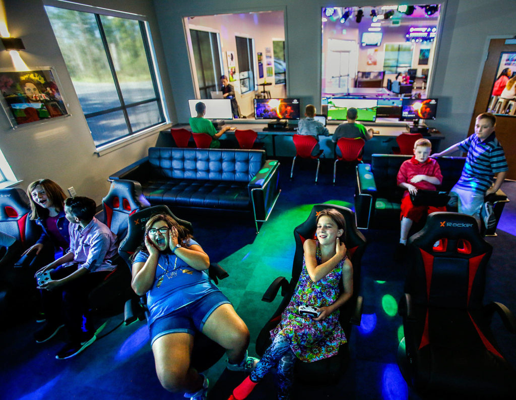 Partially bathed in blue, green and lavender light from sophisticated, programmable lighting, mostly middle-school kids enjoy playing games on big screens Thursday at the new Teen Center at the Lake Stevens Boys & Girls Club. Facing, from left, are Riley Gentry, 12, Ayden Perez, 11, Emma Price, 11, Reegan Pauley, 11, Evan Geil and his twin brother, Drew Geil, both 11. (Dan Bates / The Herald)
