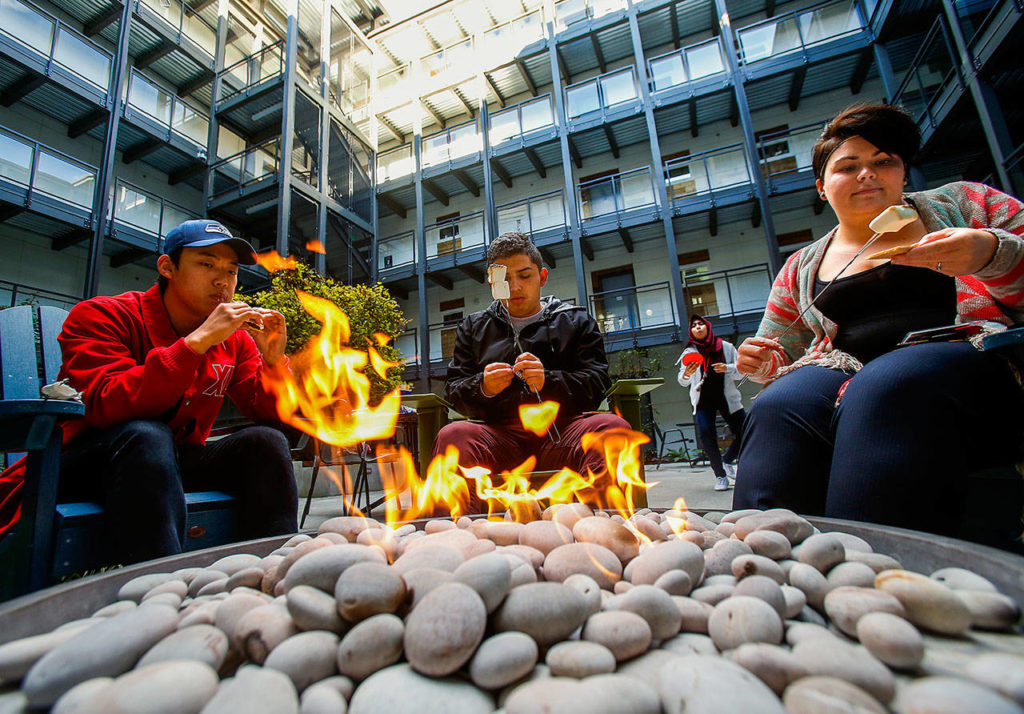 Koyo Yoshida, 18 (left), Erick Montiel, 18, and staff person Chelsea Shepherd roast marshmallows and eat s’mores next to the fire pit in the courtyard of Cedar Hall, a new student apartment complex at EvCC. (Dan Bates / The Herald)
