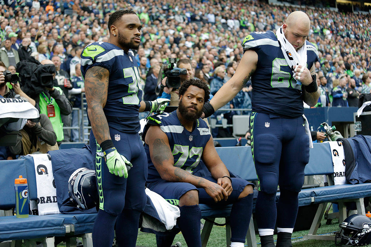 Seahawks defensive end Michael Bennett (center) is joined by teammates Thomas Rawls (left) and Justin Britt as he sits during the singing of the national anthem before a game against the 49ers on Sept. 17, 2017, in Seattle. (AP Photo/Elaine Thompson)