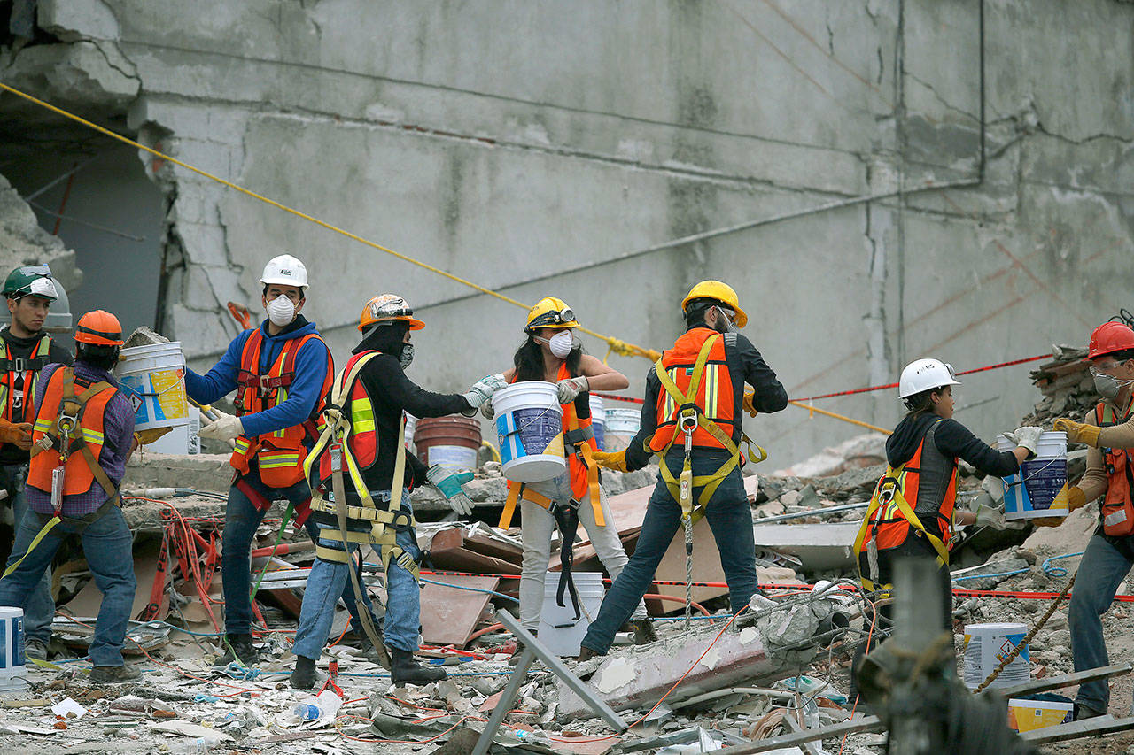 Search and rescue workers remove rubble a bucket at a time Sunday while standing on the debris of a felled office building brought down by a 7.1-magnitude earthquake, in the Roma Norte neighborhood of Mexico City. As rescue operations stretched into day 6, residents throughout the capital have held out hope that dozens still missing might be found alive. (AP Photo/Marco Ugarte)