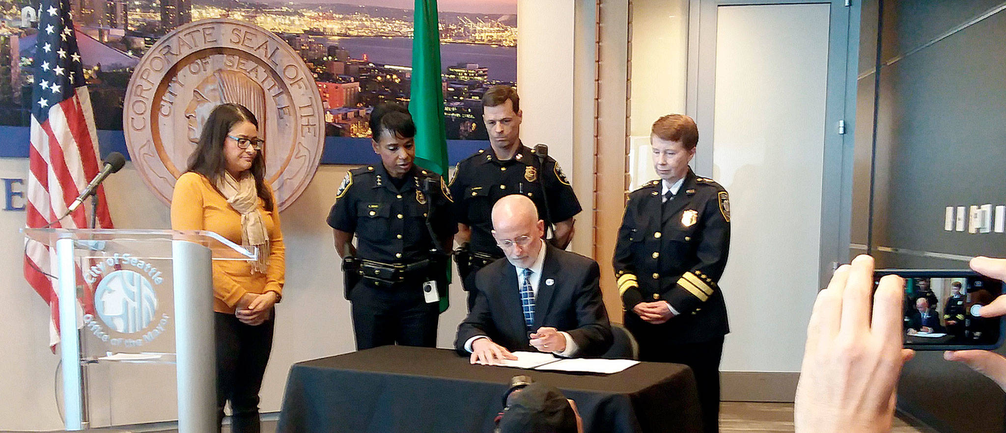 Mayor Tim Burgess signs the executive order on Wednesday to limit and begin further reform of moonlighting by Seattle police, flanked by Councilmember M. Lorena González (left) and the SPD command staff.