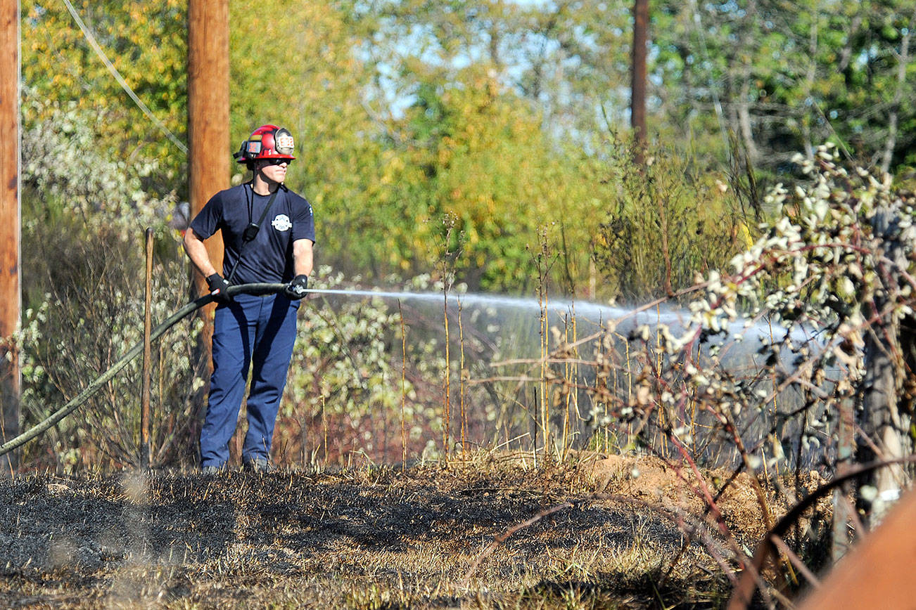 A firefighter sprays water on a few hot spots of a fire that burned in brush along the 900 block of the Ludwig Road on Thursday, Sept. 28, 2017 in Snohomish, Wa. (DougRamsay / For The Herald)