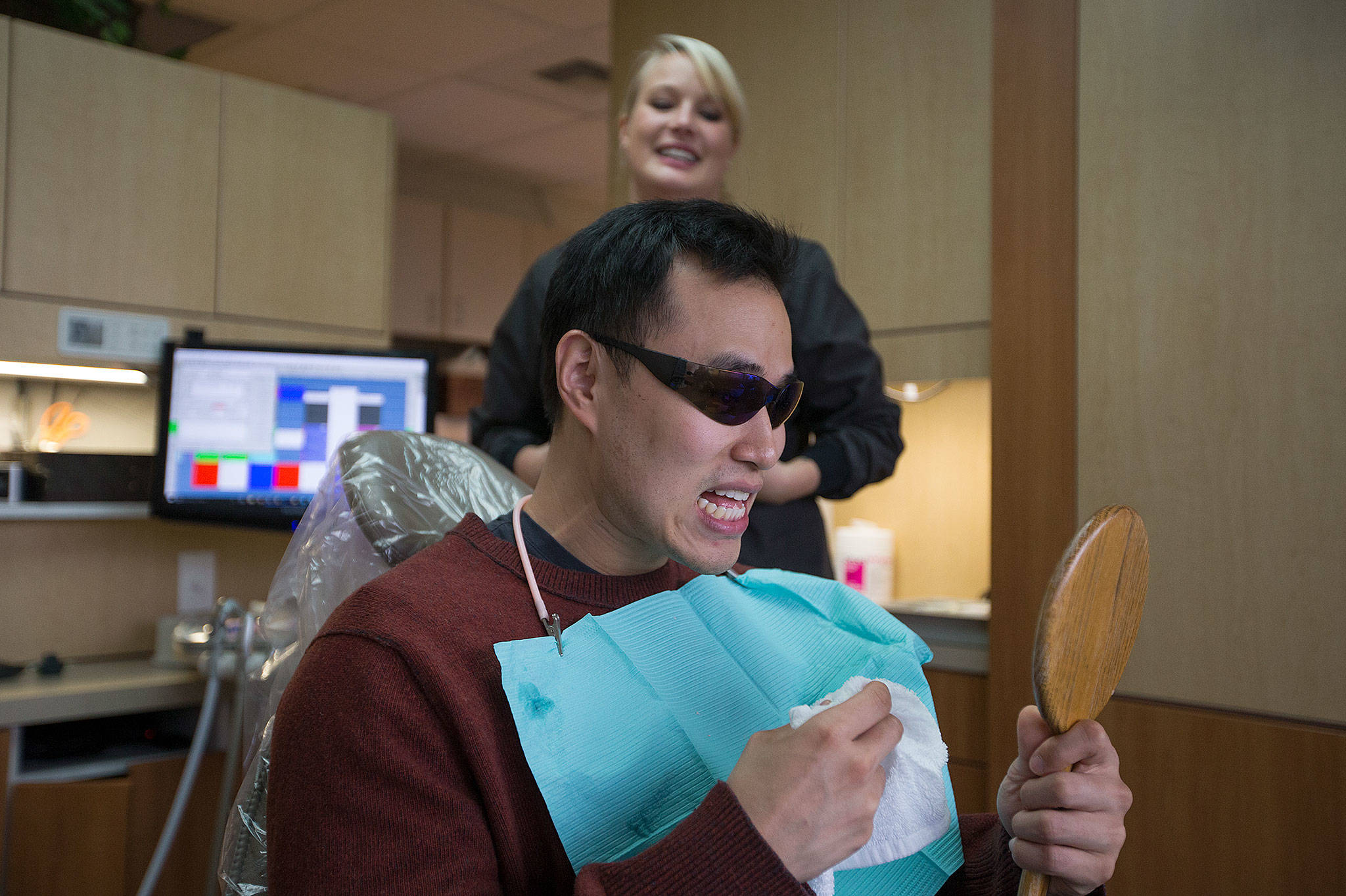 After undergoing cosmetic dental work Friday, Navy veteran Jung Hwang checks out his teeth as dental assistant Eva Russell looks on at All Smiles Northwest in Everett. (Andy Bronson / The Herald)