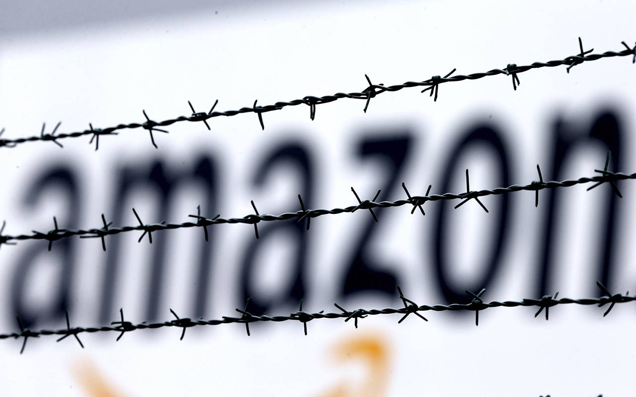 In this 2013 photo, the internet trader Amazon logo is seen behind barbed wire at the company’s logistic center in Rheinberg, Germany. (AP Photo/Frank Augstein, File)