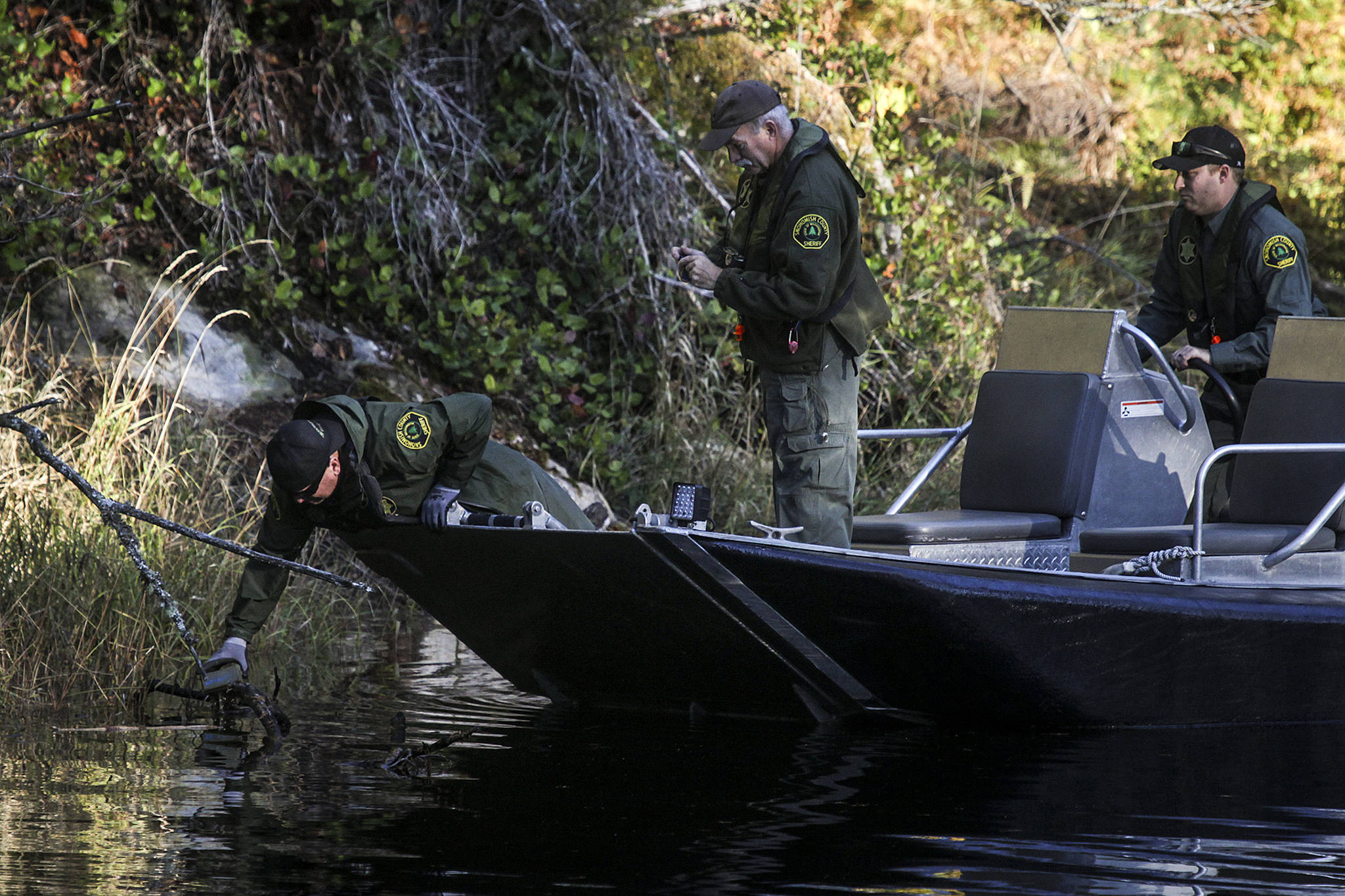Investigators comb the shore of King Lake, east of Jordan Road near Arlington, following a helicopter crash Tuesday that sent two men to the hospital with serious injuries. (Ian Terry / The Herald)