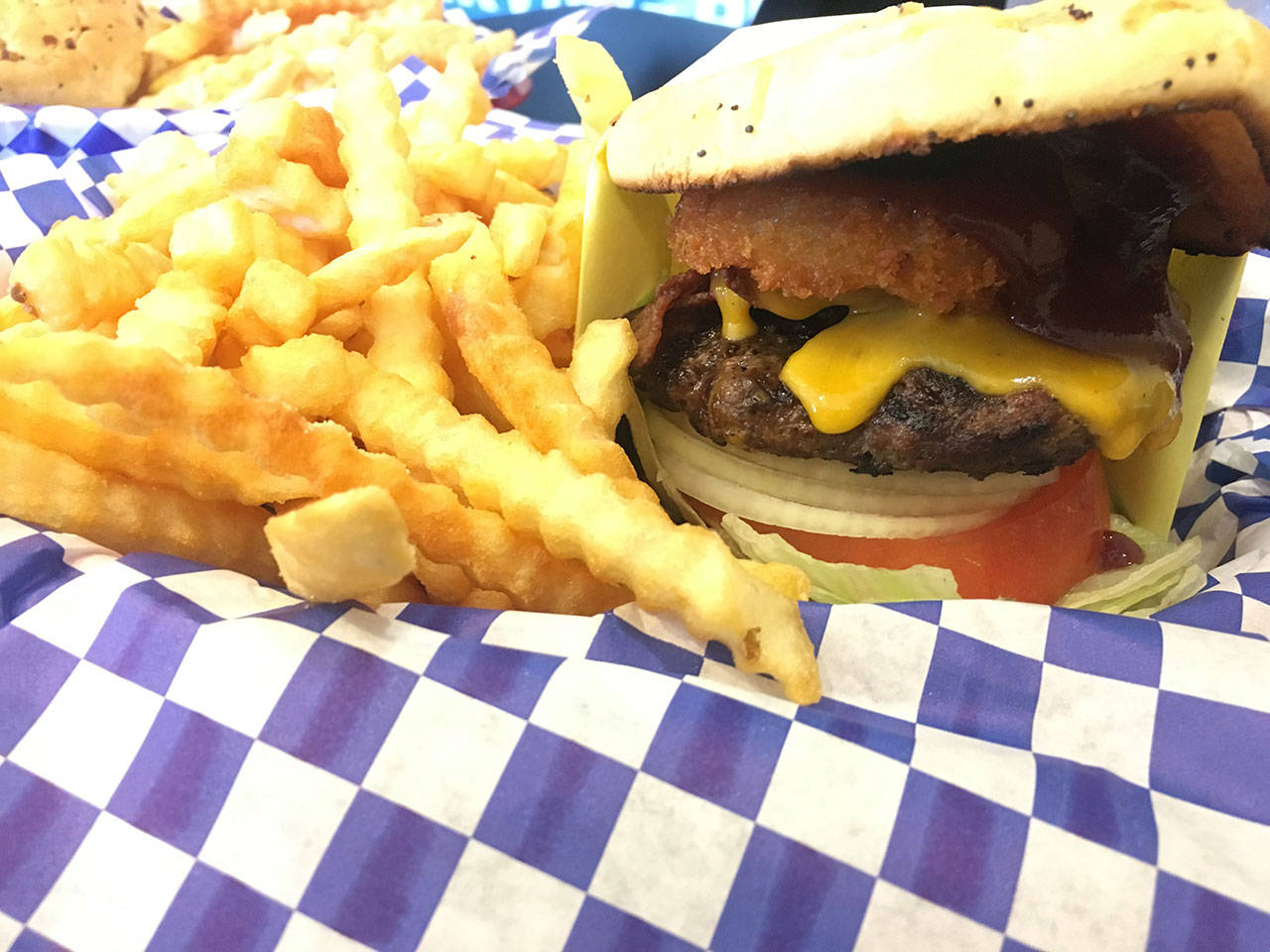 The Cowboy Burger at Burger Madness in Monroe features a pair of onion rings, BBQ sauce, bacon, cheddar cheese, hamburger patty, tomato, onion, lettuce and pickles. (Ben Watanabe / The Herald)