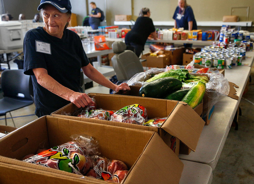 Excited about being able to serve “whole bags of apples,” volunteer Jodi Nelson watches as a crowd grows for the start of a Volunteers of America pop-up food bank in Everett. (Dan Bates / The Herald) 
