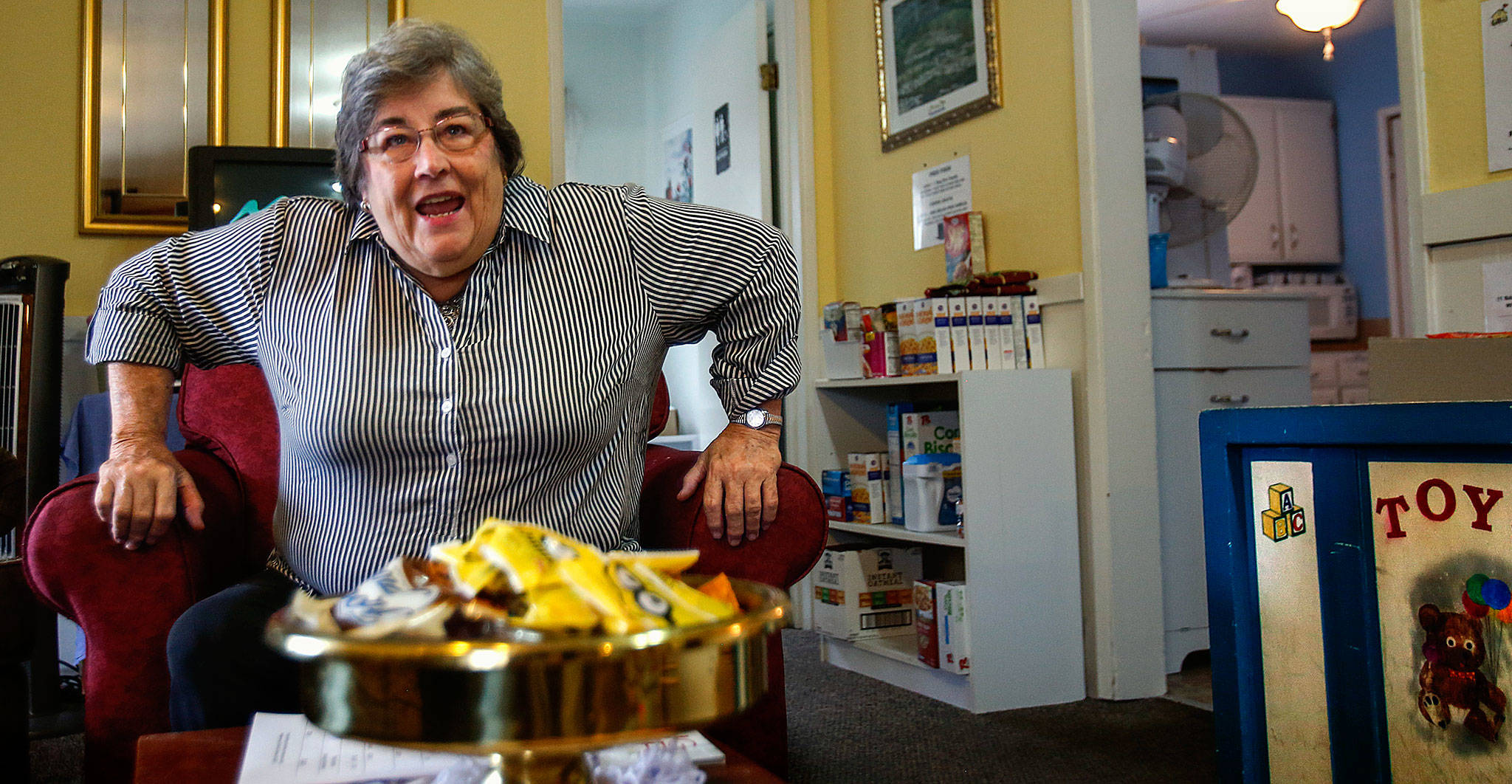 In the front room, known as the Welcome Room, Matthew House Executive Director Linda Paz jumps up from her chair to welcome volunteer Karol Bentley, who was arriving to help in the guest rooms and with family clothing and food supplies. (Dan Bates / The Herald)