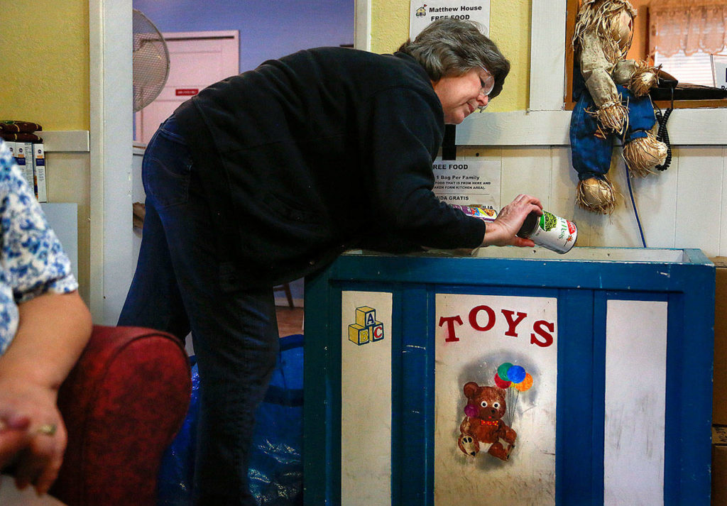Matthew House volunteer Karol Bentley looks over canned food kept in a large wooden toy box in the Welcome Room. (Dan Bates / The Herald)
