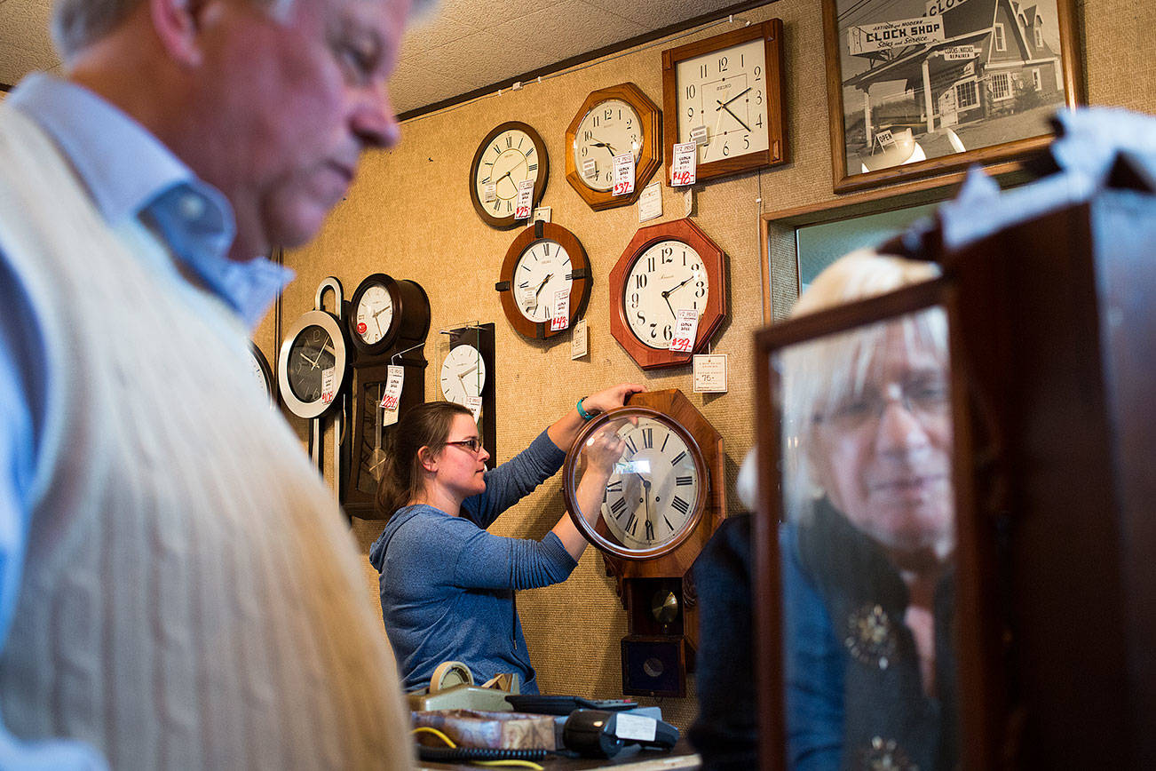 Crystal Rice, works on a customer’s clock as owner Susie Hennig, right, winds a time-and-strike clock brought in by Steve Heath at A House of Clocks on Monday, Oct. 30, 2017 in Lynnwood, Wa. The landmark Lynnwood shop plans to close after more than 54 years. David Nofziger said he and his siblings, who took over the business from their parents, are closing the shop because they’re reaching retirement age. (Andy Bronson / The Herald)