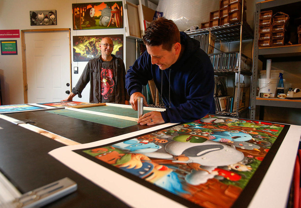 Acclaimed artist Justin Hillgrove (left) watches and talks with his assistant, Charlie Mendez recently as Mendez deals with customer print orders recently in a workroom adjacent to the studio. (Dan Bates / The Herald)
