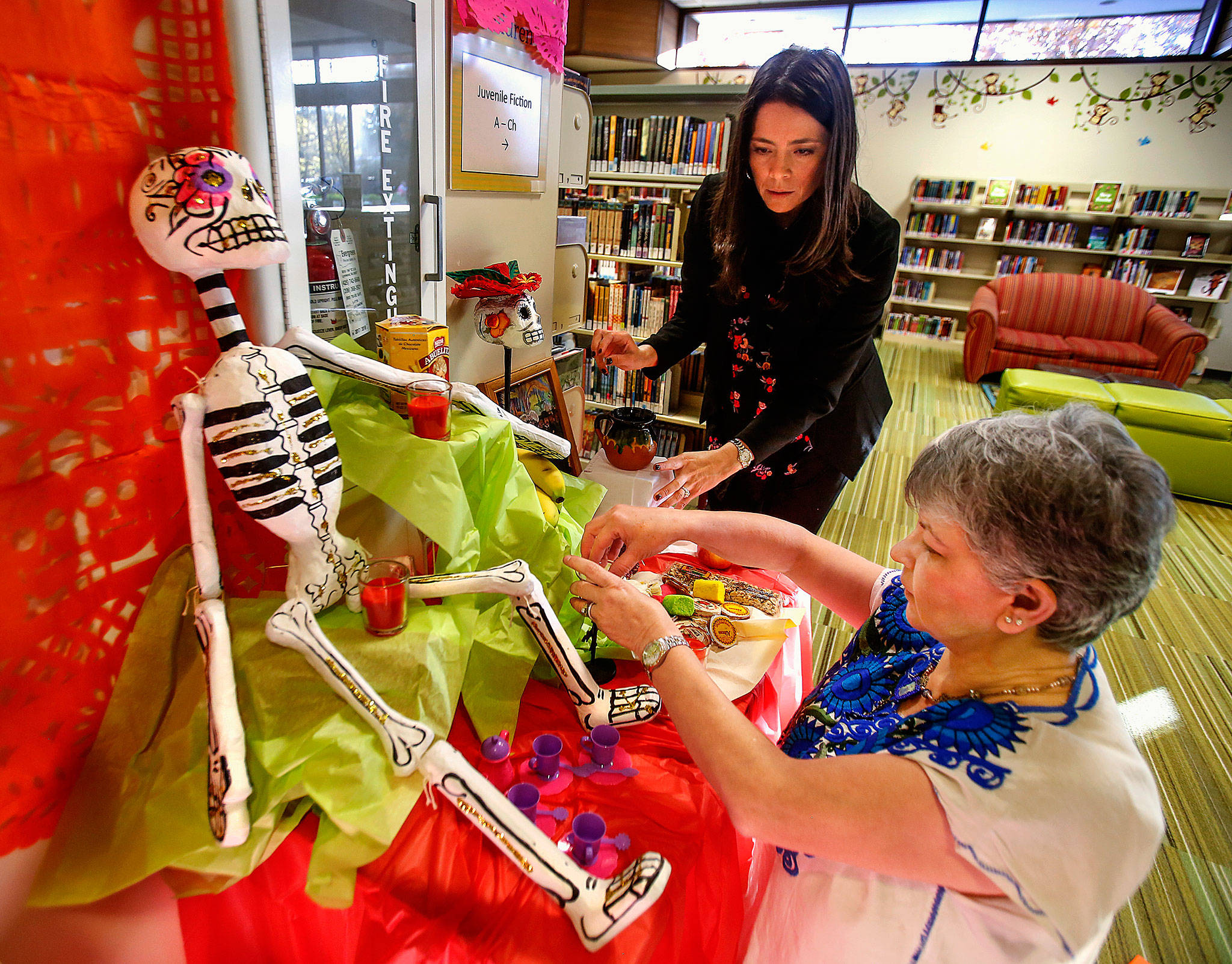 At Lynnwood Library, Julieta Altamirano-Crosby (left) and Maria Casey create a Day of the Dead display in the children’s area Tuesday. The women created a larger adult version as well. (Dan Bates / The Herald)