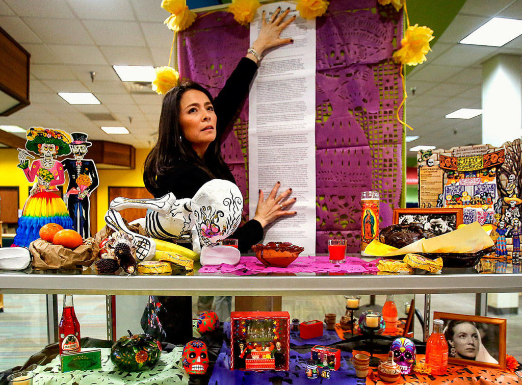 Julieta Altamirano-Crosby looks for one of her friends, Maria Casey, who is bringing her a staple gun to attach information about Day of the Dead on their display at Lynnwood Library Tuesday. (Dan Bates / The Herald)

