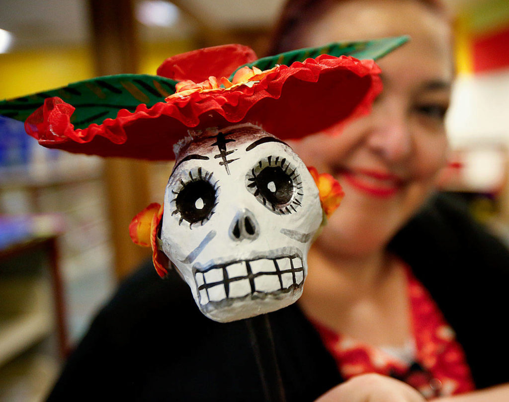 Also helping Julieta Altamirano-Crosby set up a Dia de los Muertos display in the Lynnwood Library Tuesday was Lupita Zamora, who holds up a skeleton head on a stick. (Dan Bates / The Herald)

