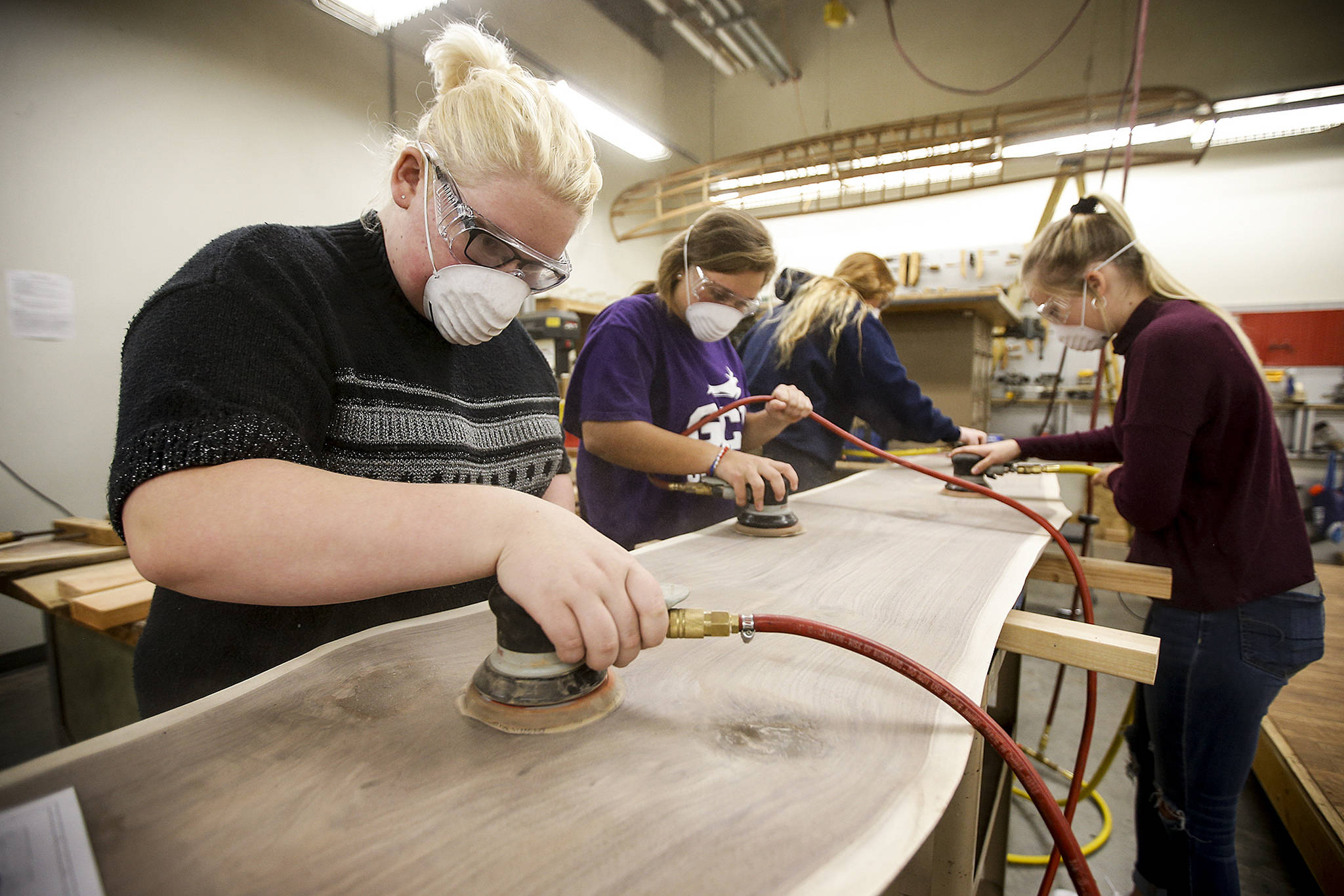 Sarah Krieg (left), sands a cut of wood that was harvested from an old walnut tree that had been recently removed on the Snohomish High School campus. Krieg and other students at the school are working to create a sofa and table from the salvaged lumber. (Ian Terry / The Herald)