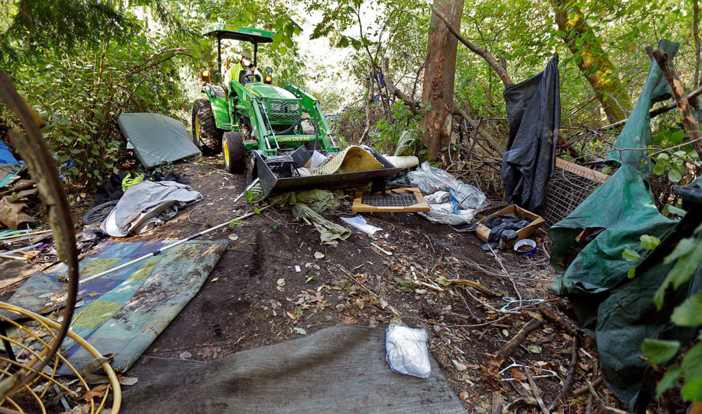A worker uses a tractor to clear a large homeless encampment in the woods near Seattle’s Ravenna Park. Residents were given notice and offered shelter beds and other services, but some people in the encampment did not remove their belongings before the cleanup began. Seattle is just one of the cities on the West Coast facing a homeless crisis of unprecedented proportions. (AP Photo/Ted S. Warren) 
