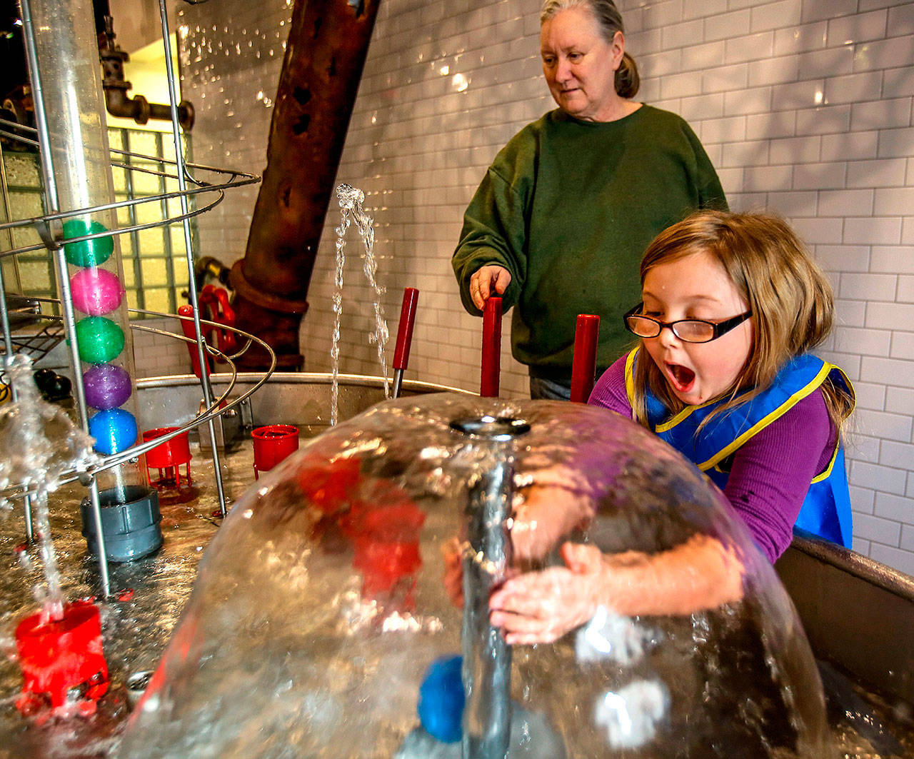 With “adopted grandmother” Michele Tanis at her side, Madison Davis, then 6, of Snohomish reacts upon discovering she can reach into an air pocket inside a water feature at the Imagine Children’s Museum in Everett in May. (Dan Bates/Herald file photo)