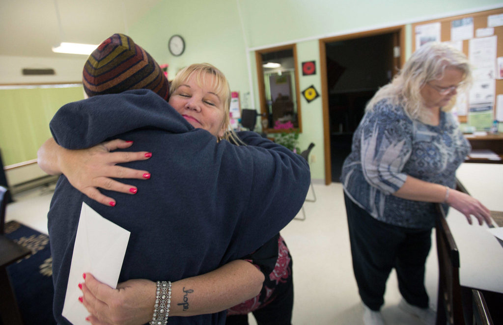 Arlington Community Resource Center Manager Peggy Ray gives Anna Y. Pritchard a hug after Pritchard drops off Thanksgiving day food on Nov. 20. Staffer Tracey Nelson (right) starts sorting the food. (Andy Bronson / The Herald)
