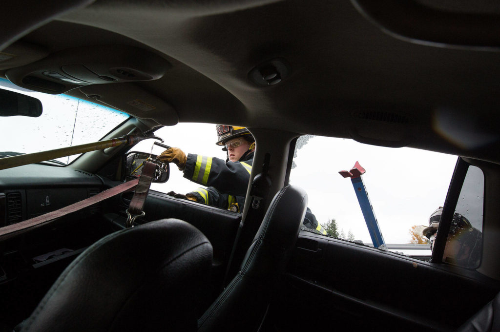 Snohomish County Fire District 19’s Dakota Herrington reaches for a strap as he helps secure an SUV sitting atop another car as Snohomish County fire departments practice multi-agency response for vehicle accidents at NW Auto Recyclers on Wednesday in Lake Stevens. Instructors from the Puyallup Extrication Team directed the training involving cars, SUVs and buses. (Andy Bronson / The Herald)
