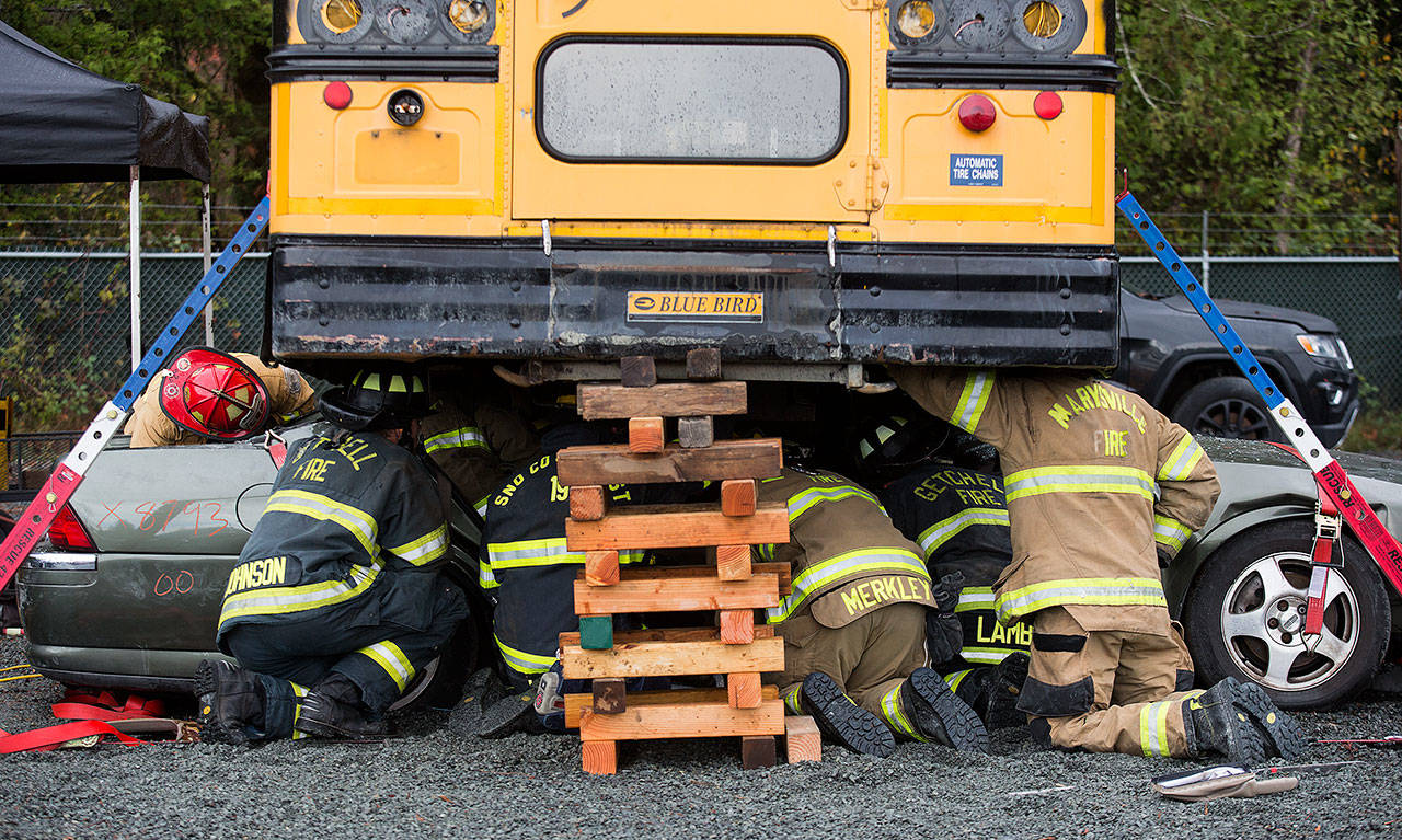 Snohomish County area firefighters crowd under a bus secured atop a car as they practice multi-agency response for vehicle accidents at NW Auto Recyclers on Wednesday in Lake Stevens. (Andy Bronson / The Herald)