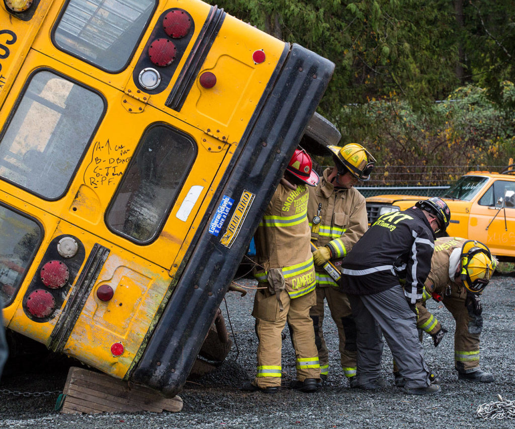 Snohomish county area firefighters brace and stabilize a rolled bus as they practice multi-agency response training for vehicle accidents at NW Auto Recyclers on Wednesday in Lake Stevens. Instructors from Puyallup Extrication Team directed the training involving cars, SUVs and even buses. (Andy Bronson / The Herald)
