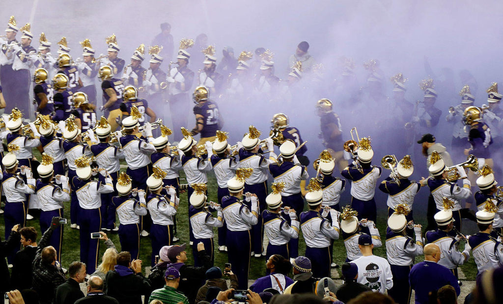 The Husky band forms walls on either side of the tunnel for the players to run out on the field through as they make their appearance prior to the start of the game. Band members min also be dreaming of games when they could play in the sunshine. (Dan Bates / The Herald)
