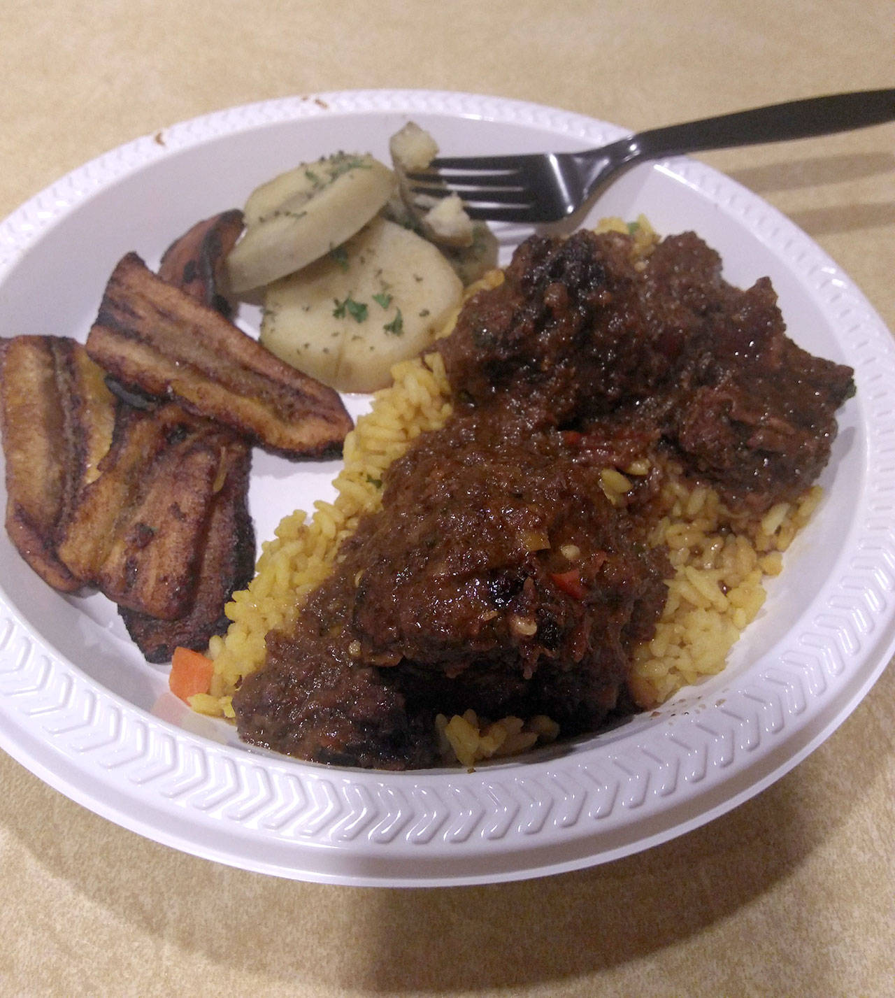 Oxtail stew with fried plantains is served on to-go tableware at Jubie’s Barbecue and Caribbean Delight in Everett. (Mary Downes / The Herald)