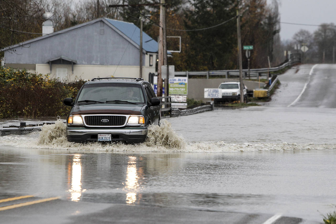 A car makes its way through a flooded area of Pioneer Highway near Hevly Road in Silvana on Wednesday. (Ian Terry / The Herald)