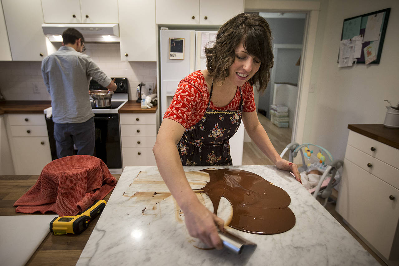 Lacey Redding spreads chocolate out on a marble slab to help control its temperature while her husband, Charlie, works at the stove in the Lynnwood couple’s kitchen. The Reddings started Church Street Chocolate in March and now sell their bars at boutique stores and coffee shops around Washington. (Ian Terry / The Herald)