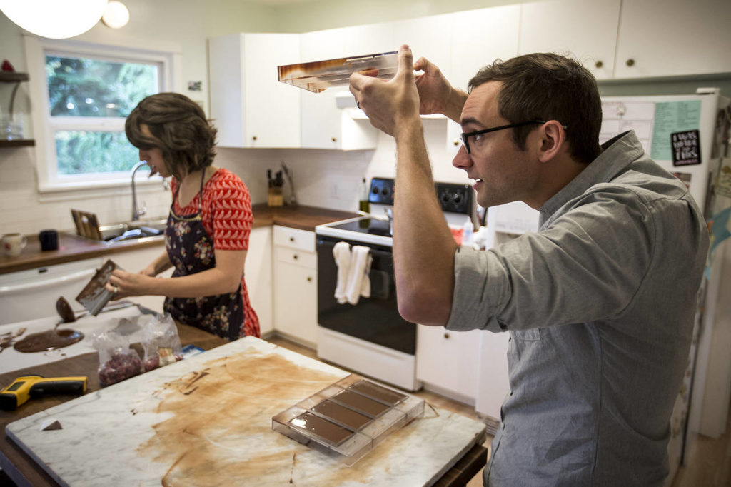 Charlie Redding (right) checks to see how completed chocolate bars are cooling as his wife, Lacey, spreads chocolate in the couple’s home. (Ian Terry / The Herald)
