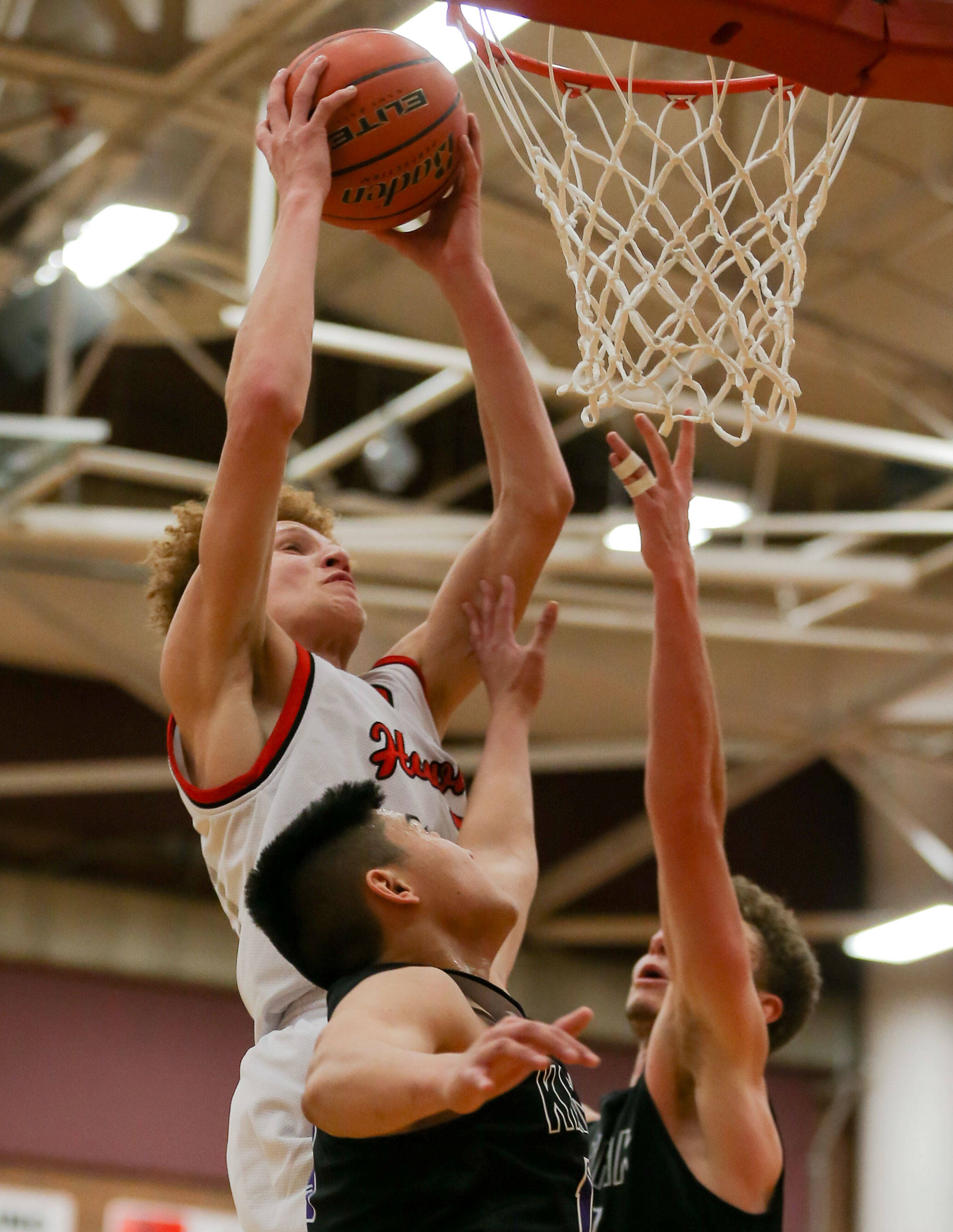Mountlake Terrace’s Khyree Armstead rebounds for a dunk over Kamiak’s Patrick Olson (bottom left) and Daniel Sharpe during a game Nov. 29, 2017, at Mountlake Terrace High School. The Hawks won 63-59. (Kevin Clark / The Herald)