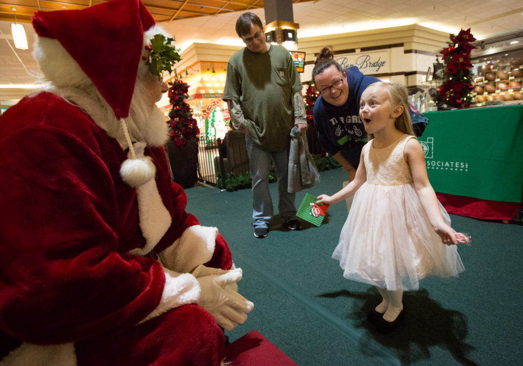 Khloe Gregory, 4, reacts with excitement with her parents Matt and Khyrsha Gregory while talking with Santa, 74-year-old Tom LaBelle, in the Everett Mall on Nov. 28. LaBelle began wearing the suit after his wife suggested he try it out. He’s now a regular each year as a mall Santa and has an entire collection of answers about Santa’s duties for his most inquisitive visitors. (Daniella Beccaria / The Herald)
