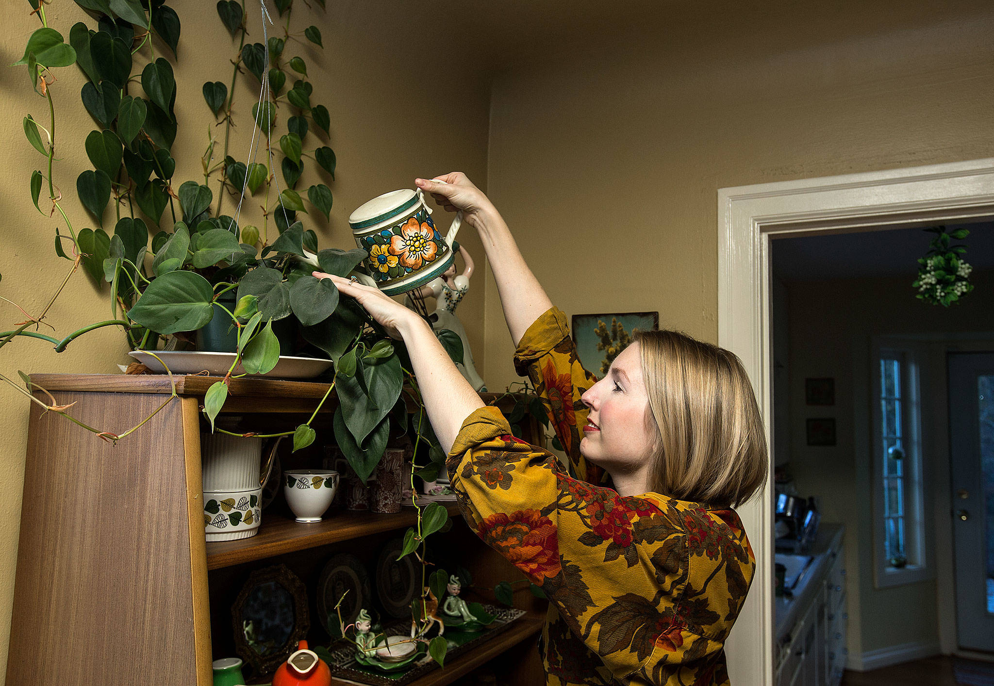 Taylor O’Brien Johnston, 32, waters a houseplant at her Everett home. With its vintage decor, her house hosts numerous low-light plants such as fern species and philodendron. (Andy Bronson / The Herald)