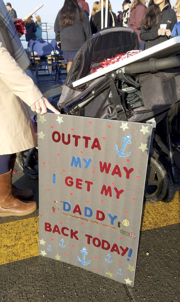 Jennifer Misner of Everett holds a sign steady for her 2-year-old daughter (in the stroller). They were at Naval Station Everett on Sunday morning to greet Misner’s husband, Zach Misner, who was returning from a six-month deployment on the USS Kidd. (Sharon Salyer / The Herald)
