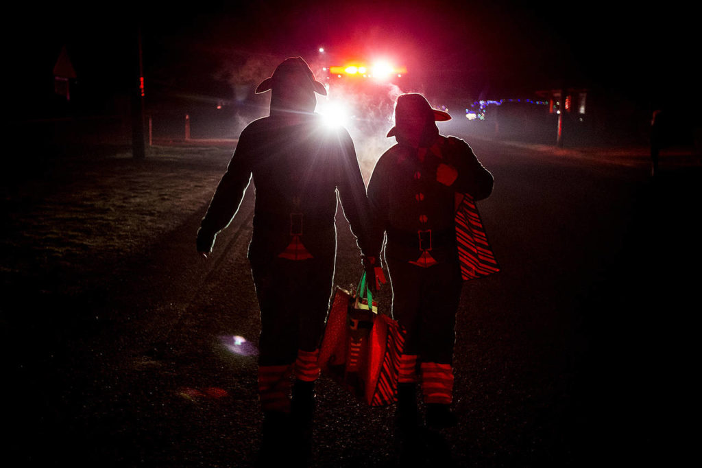 Silhoutted by the lights of a fire truck, Darrington volunteer firefighters Angela Botamanenko and Tim Ziesemer walk through town on Tuesday, Dec. 12 while handing out candy canes for the annual Christmas Parade. (Ian Terry / The Herald)
