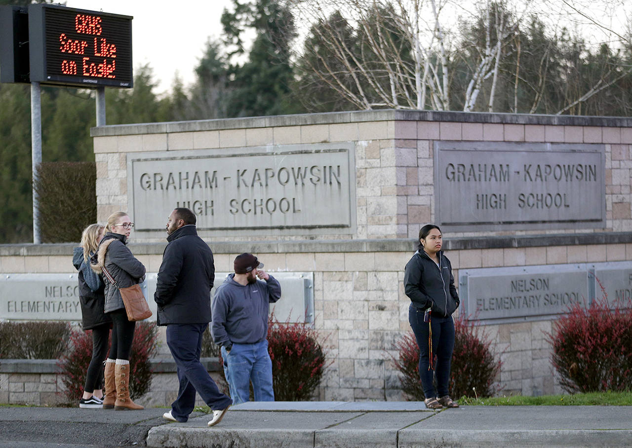People wait to be reunited with students on lockdown near a sign for Graham-Kapowsin High School, Frontier Middle School, and Nelson Elementary School on Tuesday in Graham. (AP Photo/Ted S. Warren)