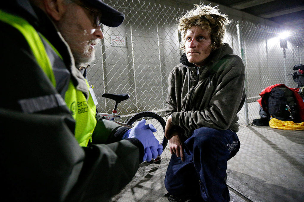 Alex Rehn (right), a homeless heroin and meth addict, talks with a volunteer with MercyWatch, an outreach group that serves the needs of the homeless population in Everett, as they kneel on a sidewalk under the Smith Avenue Bridge. Rehn, who has since entered a treatment program, said his addiction had destroyed everything he once had, including a job and time with his young son. “It’s a deep dark ugly hole that tricks your mind into believing it’s not what it really is,” Rehn said. (AP Photo/Ted S. Warren) 
