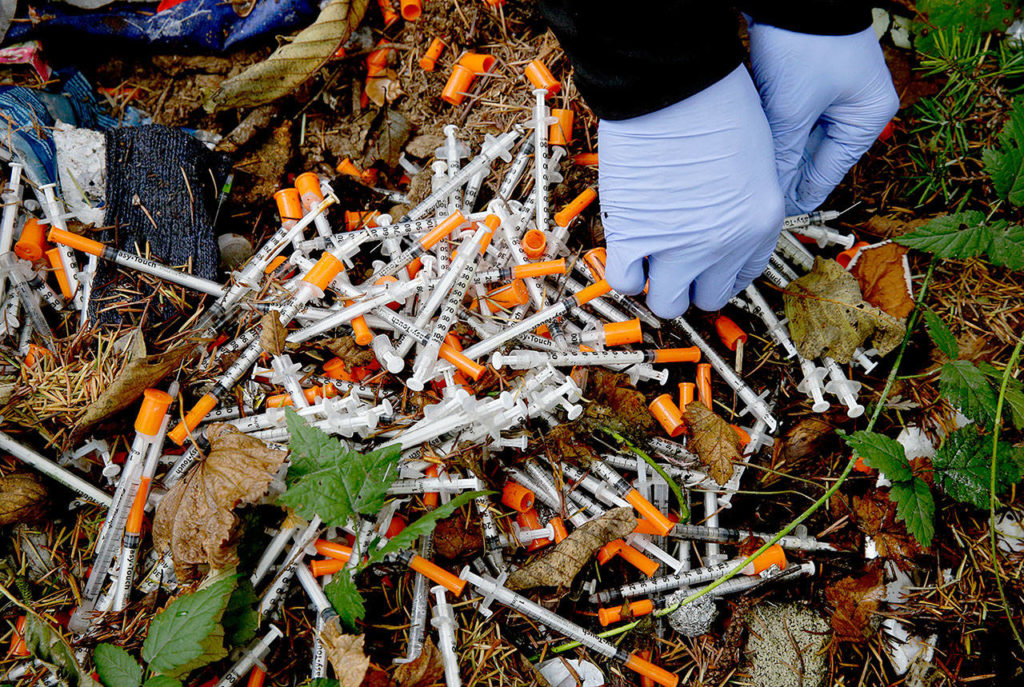 Steph Gaspar, a volunteer outreach worker with The Hand Up Project, cleans up needles used for drug injection that were found at a homeless encampment in Everett. (AP Photo/Ted S. Warren) 
