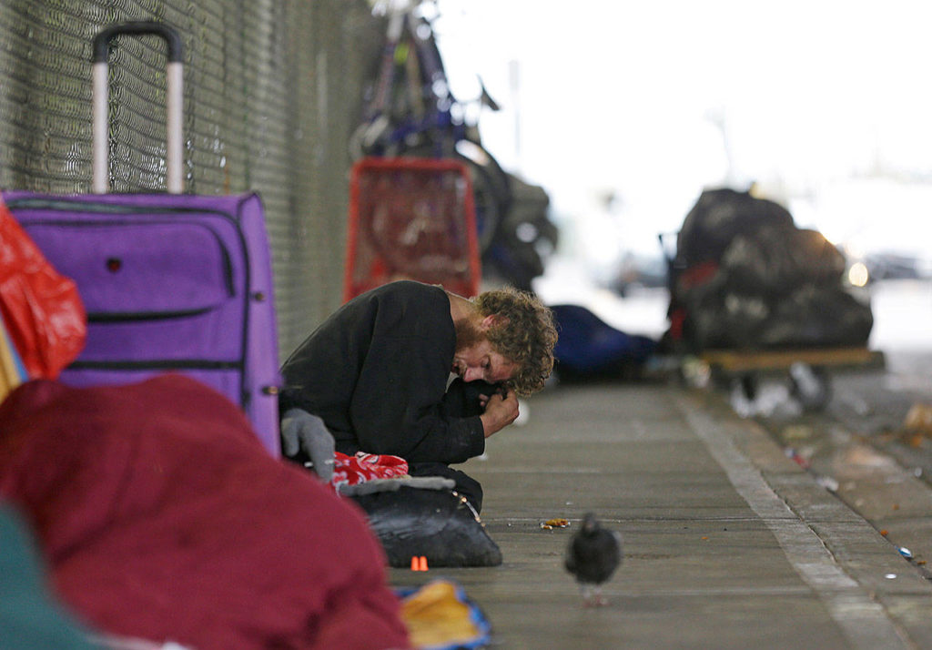 Dominic, who lives with mental illness, sits on a sidewalk under the Smith Avenue Bridge in Everett. He has been identified as one of the top chronic and costliest users of emergency and other services, but despite the efforts of a specialized team of experts, he remains on the streets. (AP Photo/Ted S. Warren)
