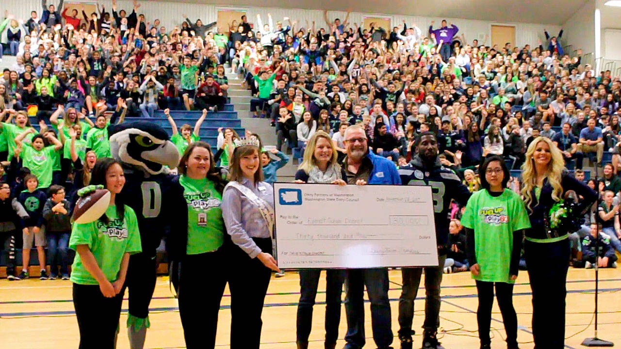 Washington State Dairy Ambassador Anna Teachman (in crown) (from left), Monroe dairy farmers Jim and Dolores Werkhoven, and Seattle Seahawk Marcus Trufant present a $30,000 check to Gateway Middle School at a Nov. 28 assembly. (Contributed photo)