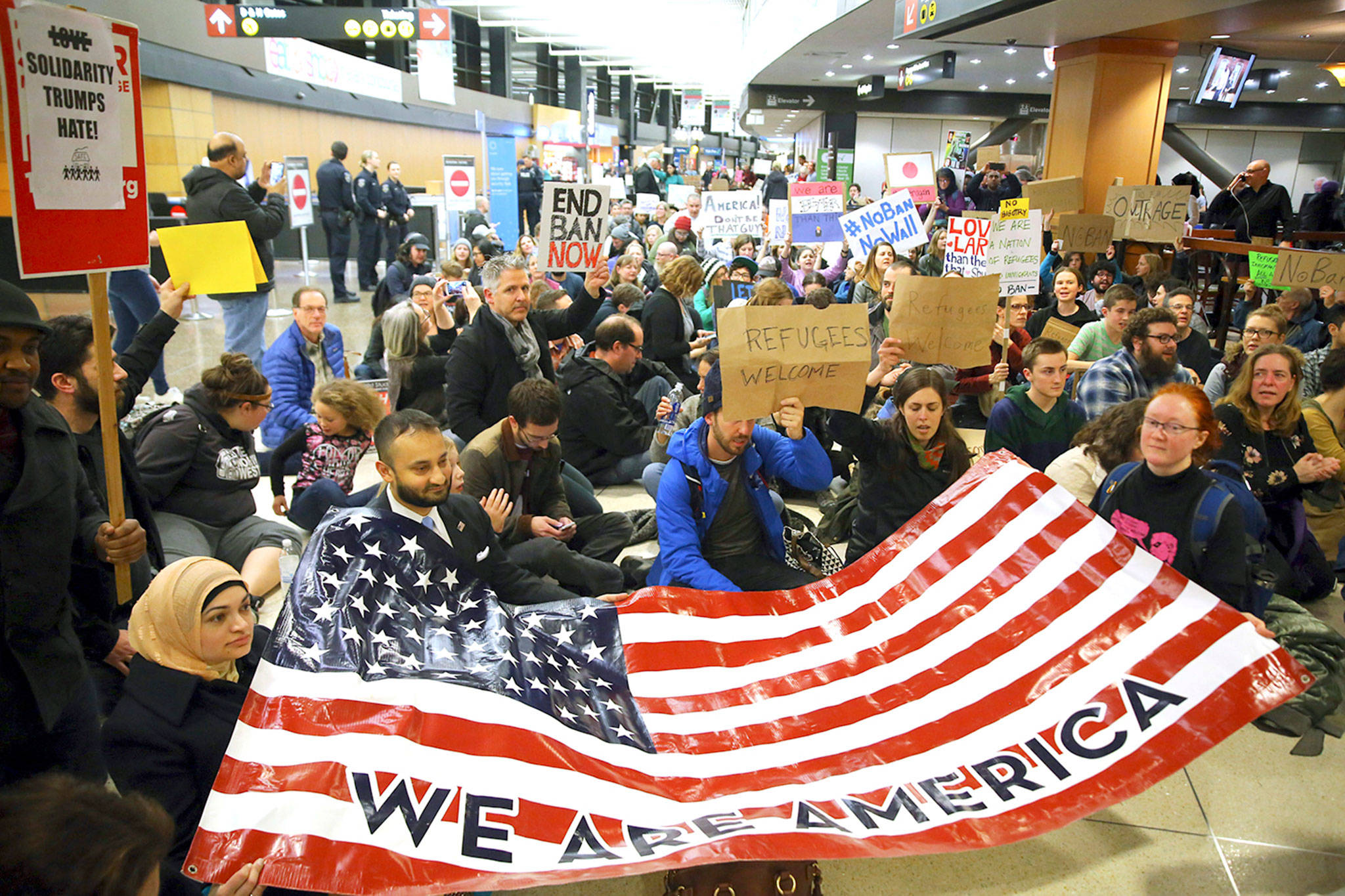 In this Jan. 28, 2017 photo, demonstrators sit down in the concourse and hold a sign that reads “We are America,” as more than 1,000 people gather at Seattle-Tacoma International Airport to protest President Donald Trump’s order that restricts immigration to the U.S. (Genna Martin/seattlepi.com via AP, File)