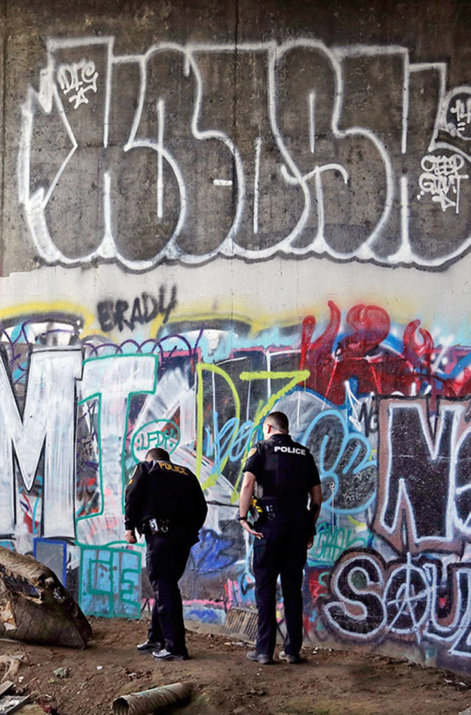 Police Sgt. Mike Braley (left) and officer Kevin Davis walk along the bottom of a highway overpass in Everett — a known location for drug use. (Elaine Thompson/The Associated Press)
