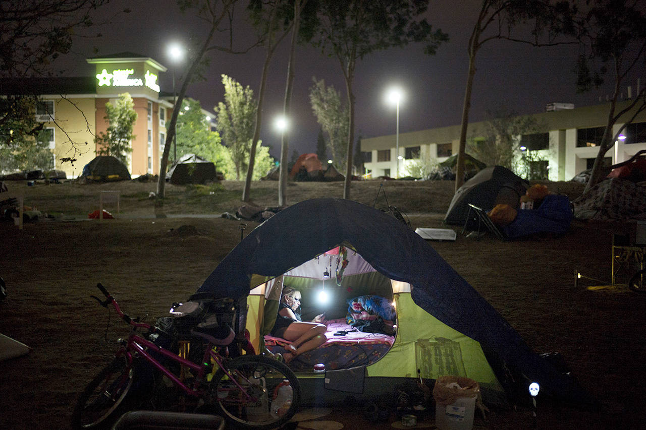 Homeless Jacqueline Anderson, 63, passes time playing with her smartphone in a homeless encampment on the Santa Ana River trail on Dec. 10 in Anaheim, California. “I like it here,” said Anderson who had been to a few other encampments before settling on the river trail. “People always bring you food.” (AP Photo/Jae C. Hong)