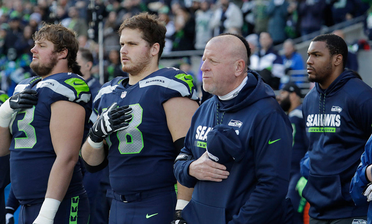 Seattle Seahawks assistant head coach and offensive line coach Tom Cable stands with players during the singing of the national anthem before Sunday’s game against the Arizona Cardinals. (AP Photo/Elaine Thompson)