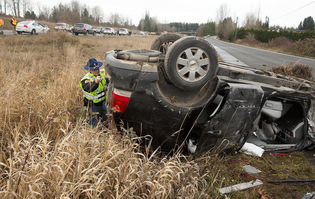 A Washington state trooper pulls the license plate off an overturned SUV after a six-vehicle pileup on U.S. 2 that caused serious injuries and shut down the road in both directions on Monday near Snohomish. (Andy Bronson / The Herald) 
