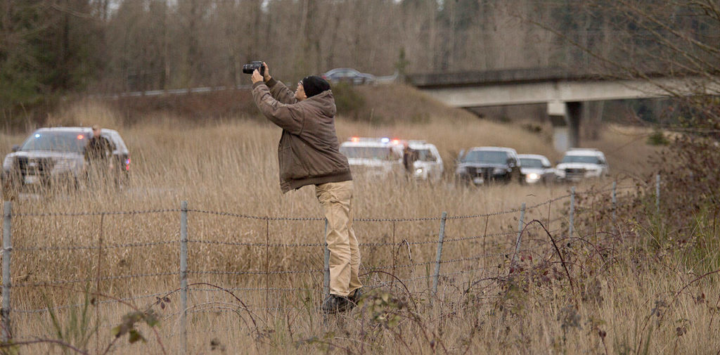 A man stands on a barbed-wire fence to get a better photo of a six-vehicle pileup on U.S. 2 that caused serious injuries and shut down the road in both directions on Monday near Snohomish. (Andy Bronson / The Herald)

