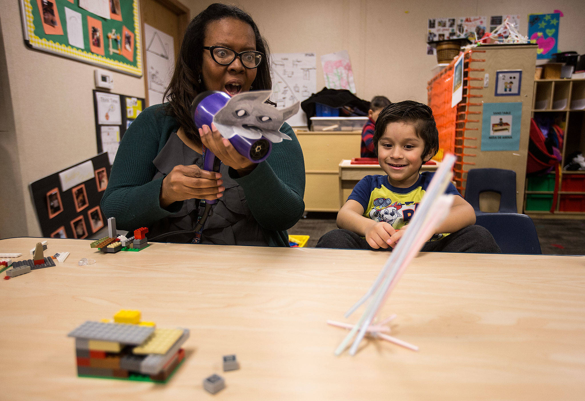 Lowell Elementary teacher Erin Marrow uses a blow dryer to represent the Big Bad Wolf to move a straw house across the table as Giovanni De Jesus Olmos watches Thursday in Everett. Using the theme of “The Three Little Pigs,” early learning students use STEM practices to build and test model houses built from straws, popsicle sticks and LEGO bricks. (Andy Bronson / The Herald)