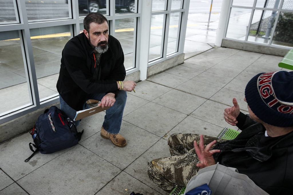 Volunteer Paul Olson (left), of Everett, completes a survey with a man at a bus stop on Smokey Point Boulevard on Tuesday. Olson, a former U.S. Army infantryman, was homeless for two months following his time in the military. (Ian Terry / The Herald)

