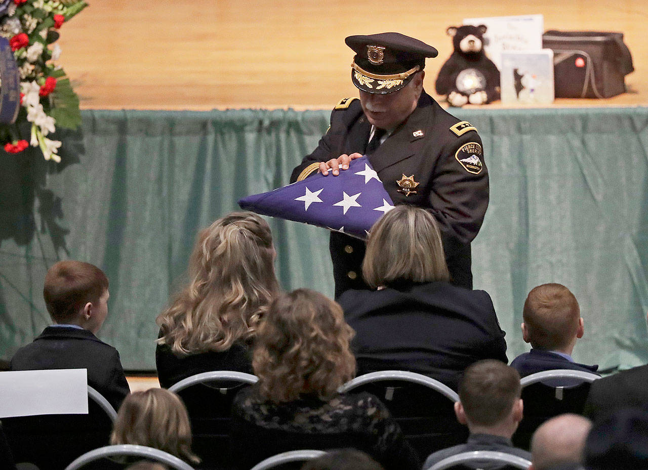 The U.S. flag that covered the casket bearing slain Pierce County Sheriff’s Deputy Daniel McCartney is presented to family members, Wednesday during a memorial service at Pacific Lutheran University in Tacoma. McCartney died the night of Jan. 7 after being shot while responding to a to a break-in call southeast of Tacoma. (AP Photo/Ted S. Warren, Pool)